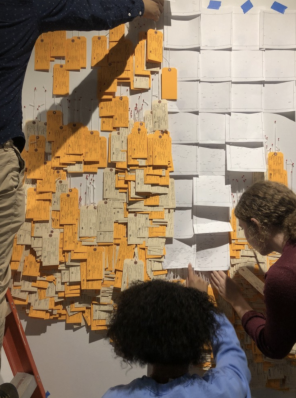 Two people place toe tags on the exhibit wall grid