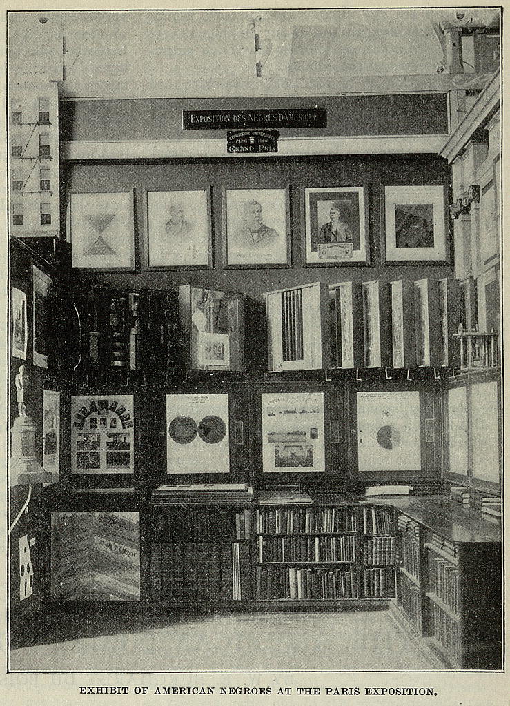 Photo of exhibit table with charts, graphs and photos mounted in frames along three walls, depicting elements Black American life during the late 19th and early 20th centuries.