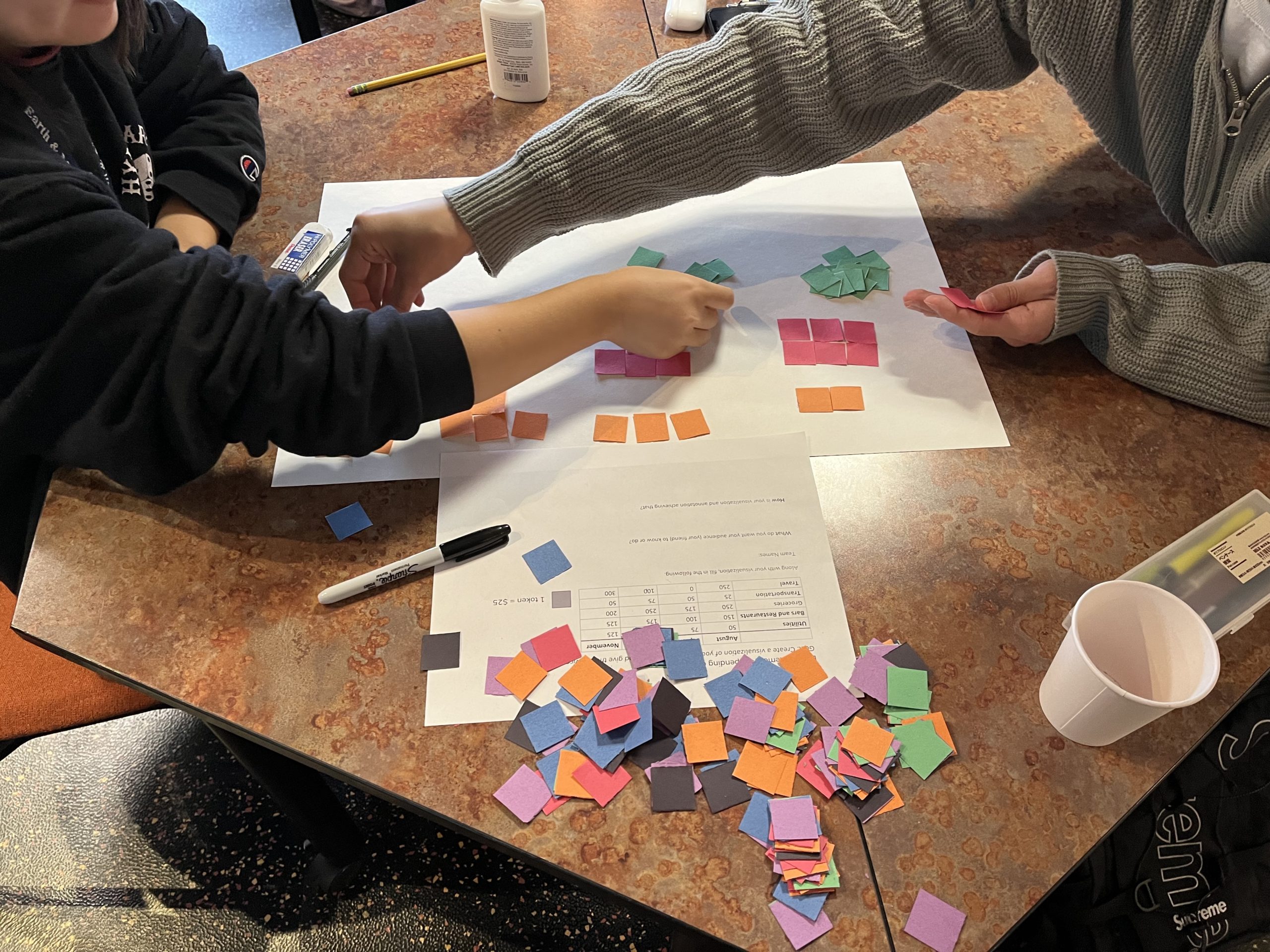 Photo of students grouping colored squared pieces of paper together on a table.
