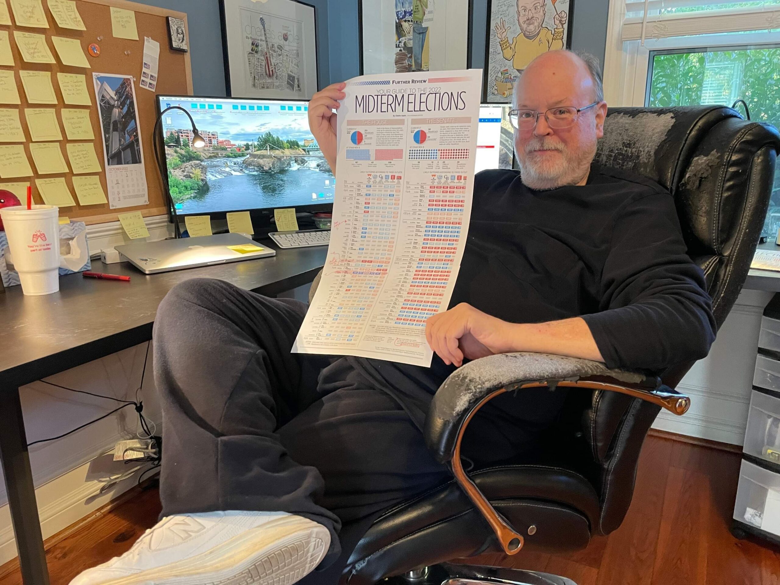 Photo of Charles Apple at his desk, holding a printed infographic about the U.S. midterm elections.