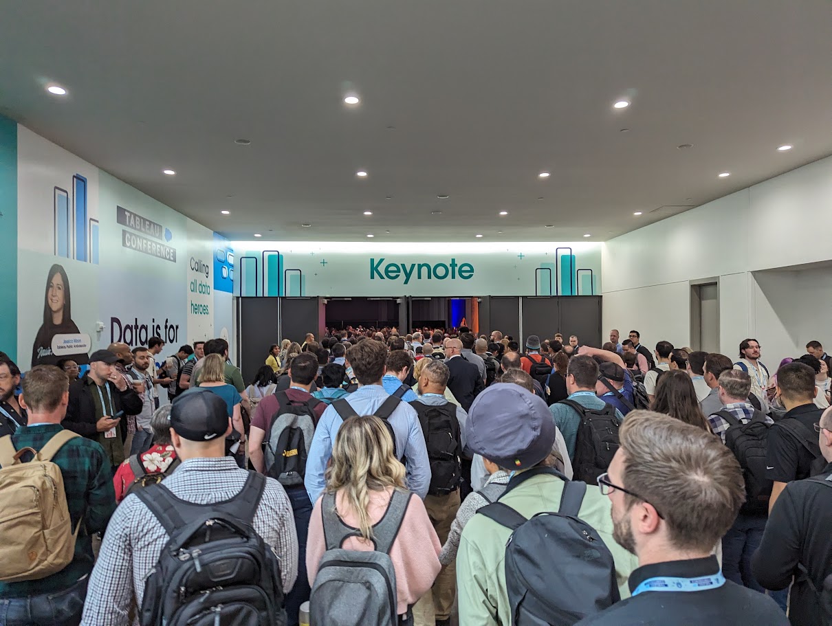 100 or so people, most with backpacks, enter a large conference space simultaneously through industrial doors. The text above the doors reads, 'Keynote.'" Comment, "Tableau Conference is large and you feel it most in moments of conference-wide learning. This is a picture of everyone heading in for the keynote presentation.